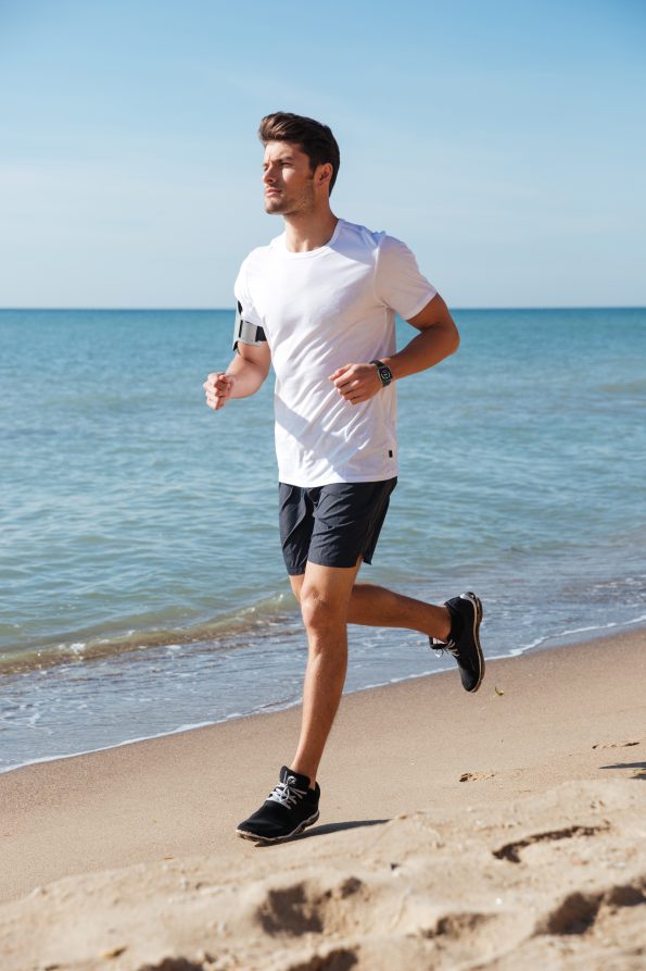 Concentrated young sportsman jogging on the beach